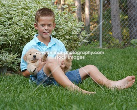 boy with golden retriever pup in garden