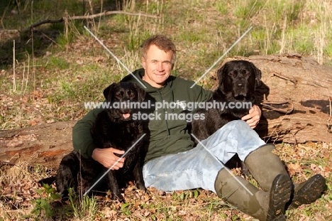 man sitting in field with two black labradors